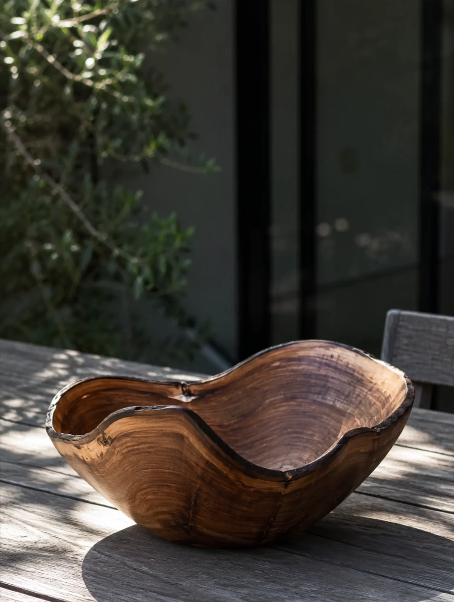 Undulating hand-turned wooden vessel in dappled outdoor light.